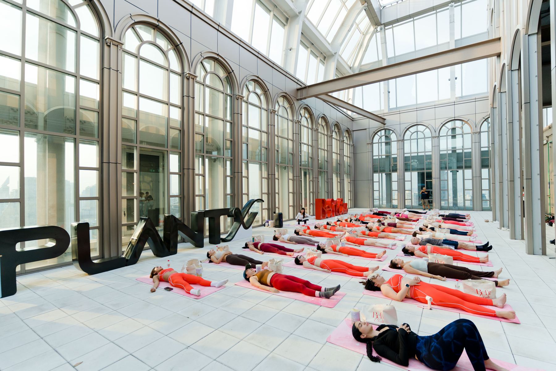 A large group lying on mats during a sound bath in a glass roofed hall