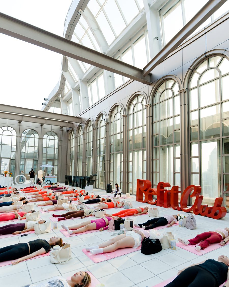 A brand collaboration sound bath in a glass roofed hall, guests lying on mats beside the sponsor lettering