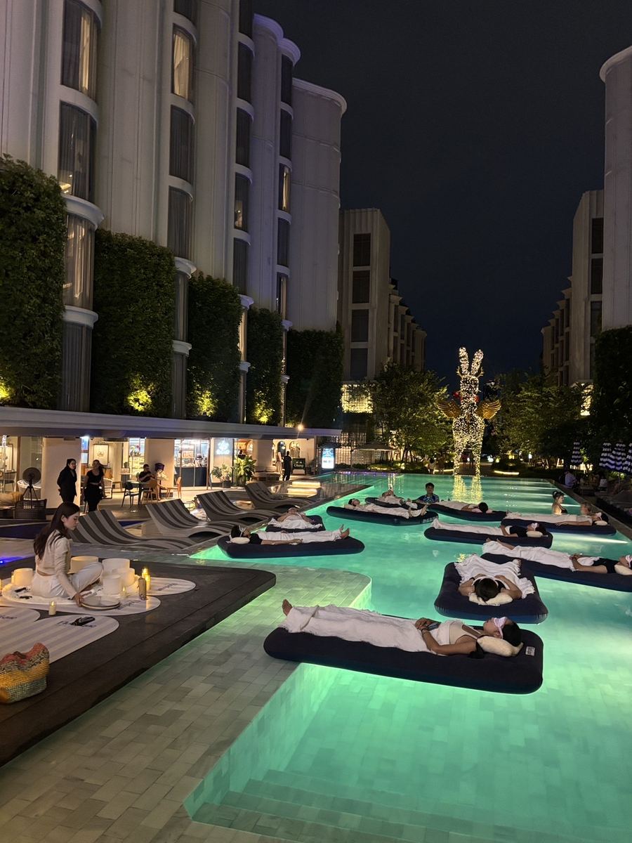 Floating beds laid out on a lit hotel pool at night with the property behind