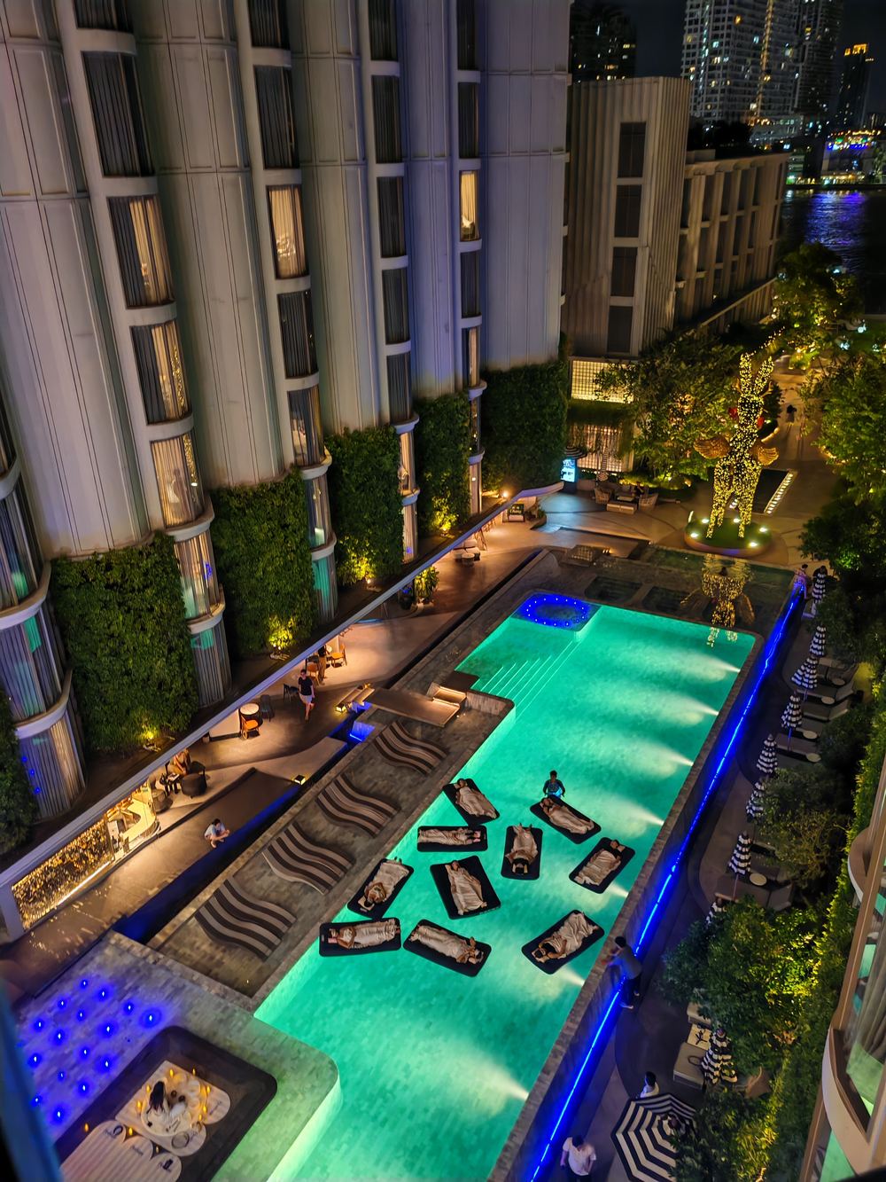 An overhead view of a hotel pool laid out with floating beds and candlelight for a floating sound bath