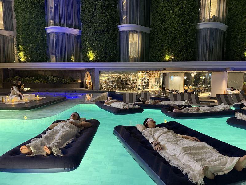 Guests resting on floating beds in a pool during a floating sound bath in Thailand