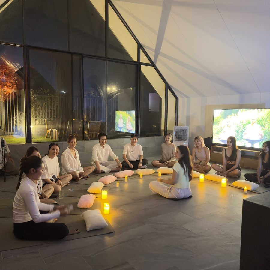 A facilitator leading a seated circle of guests on cushions for a group sound healing session
