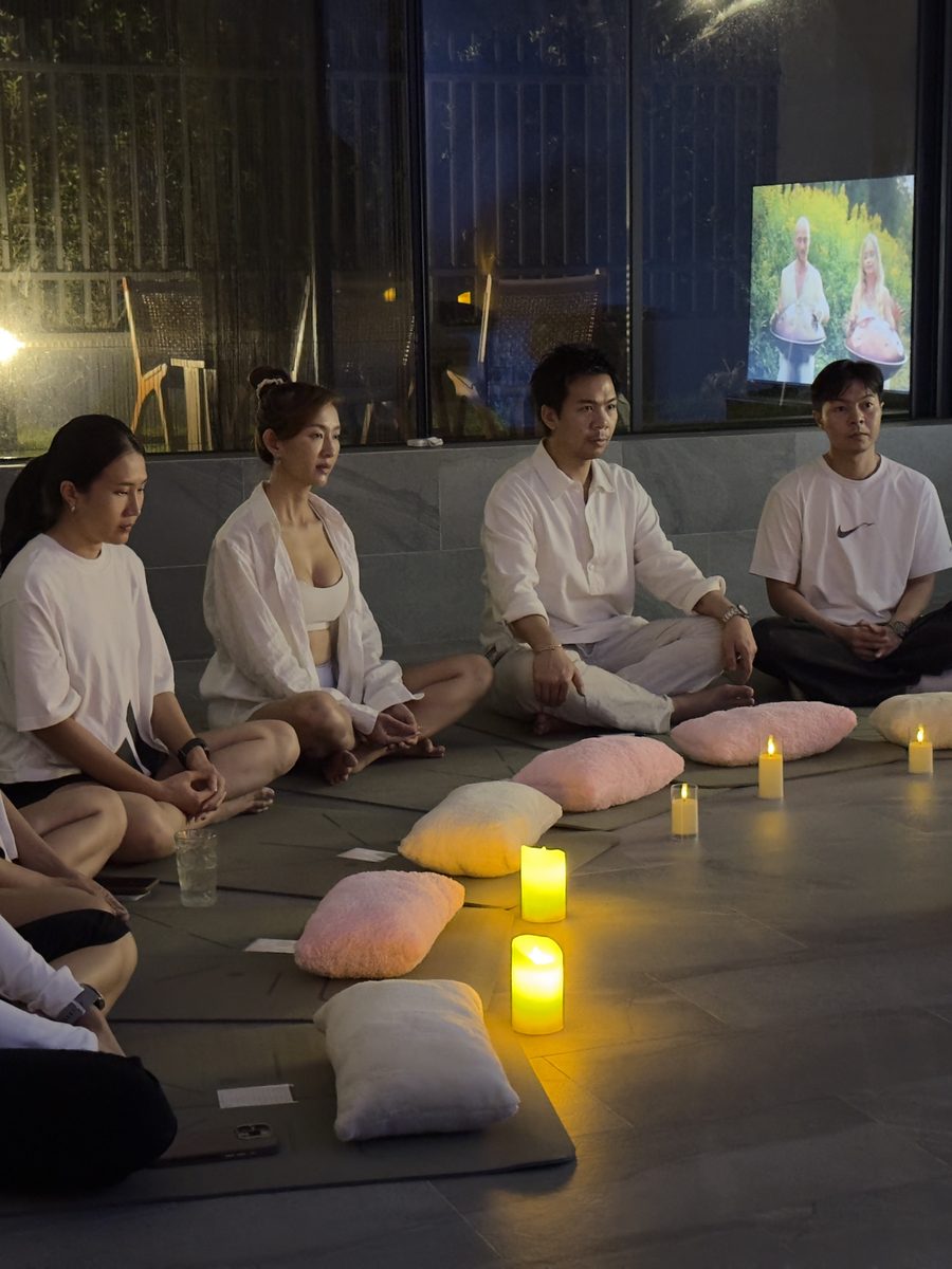 Guests seated in a circle on mats and cushions around candlelight before a group sound journey