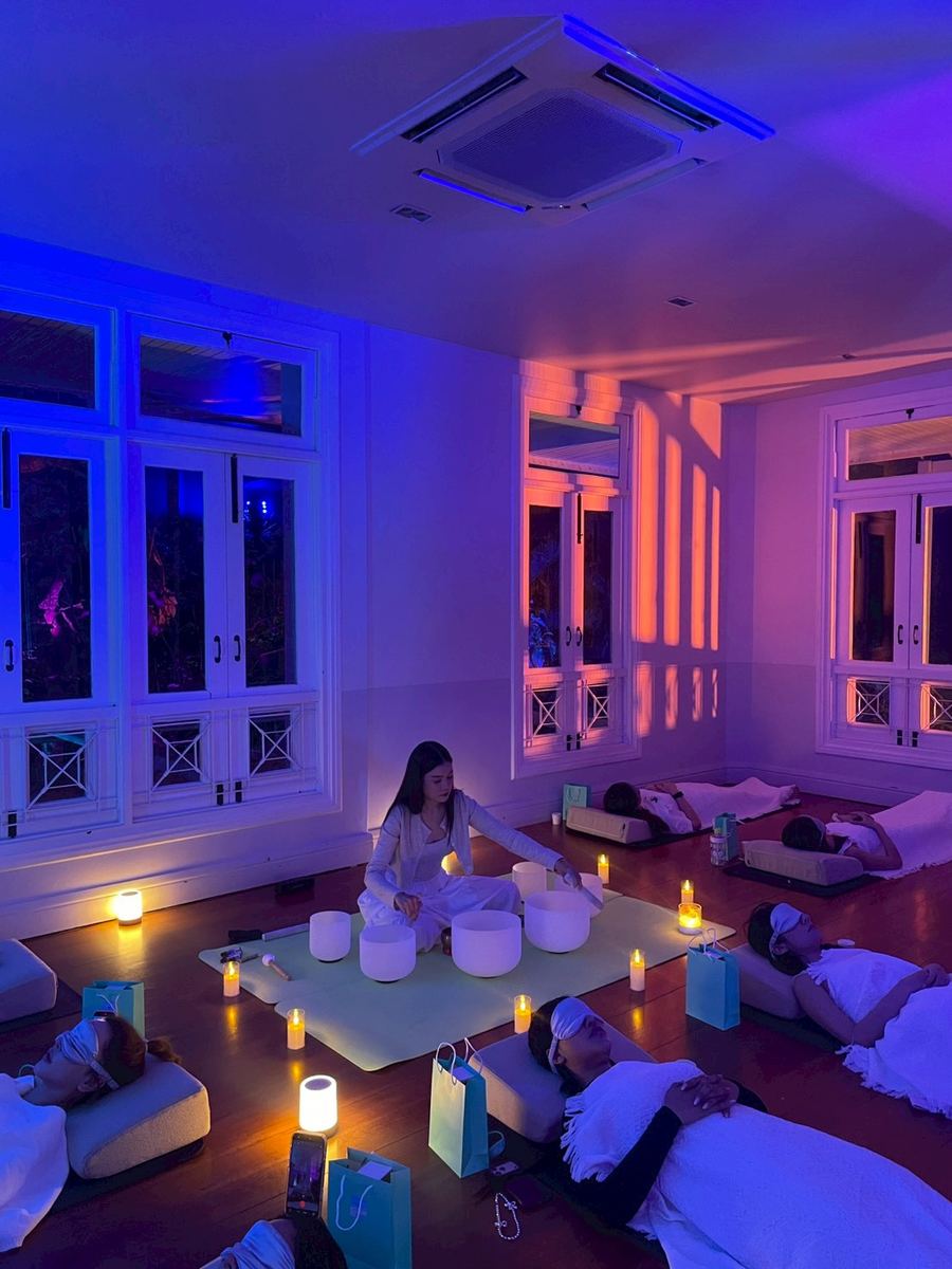 Guests resting on mats around a low table of singing bowls at a private indoor sound bath